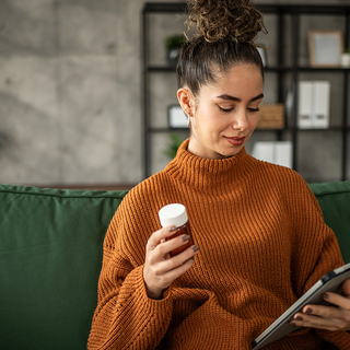 Junge Frau nimmt Medizin und recherchiert die Nebenwirkungen auf ihrem Tablet.