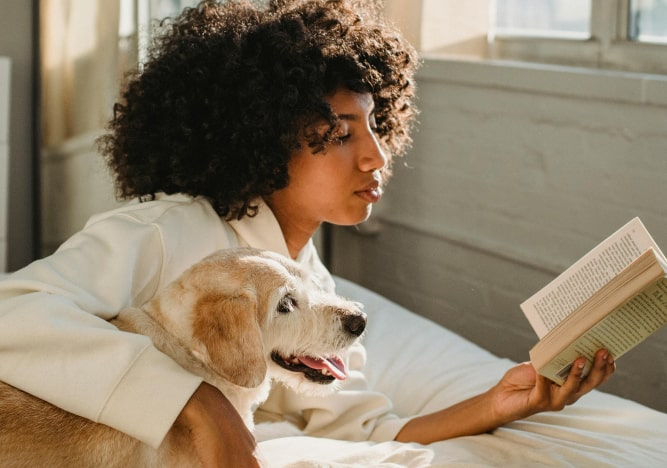 Junge Frau mit Hund liest zu Hause ein Buch