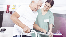&Auml;lterer Mann an einer Gehilfe, betreut von einer Krankenschwester