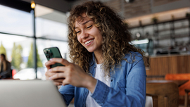Junge l&auml;chelnde Frau mit Handy in der Hand