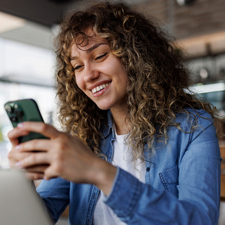 Junge l&auml;chelnde Frau mit Handy in der Hand