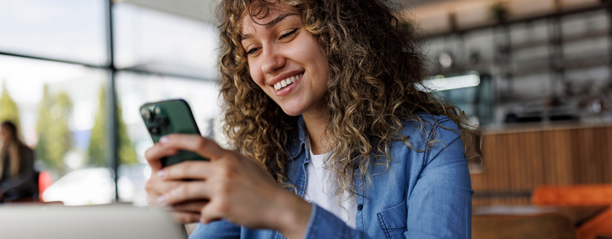 Junge l&auml;chelnde Frau mit Handy in der Hand