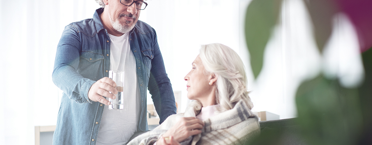 Mann reicht einer &auml;lteren Frau ein Glas Wasser
