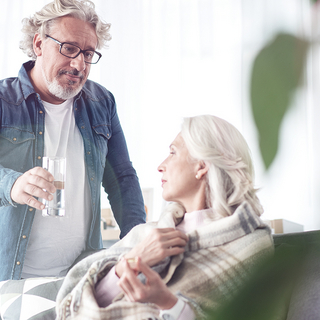 Mann reicht einer &auml;lteren Frau ein Glas Wasser