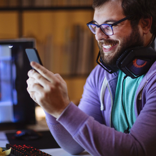 Ein nerdiger Mann mit Bart schaut auf sein Smartphone, l&auml;chelt.