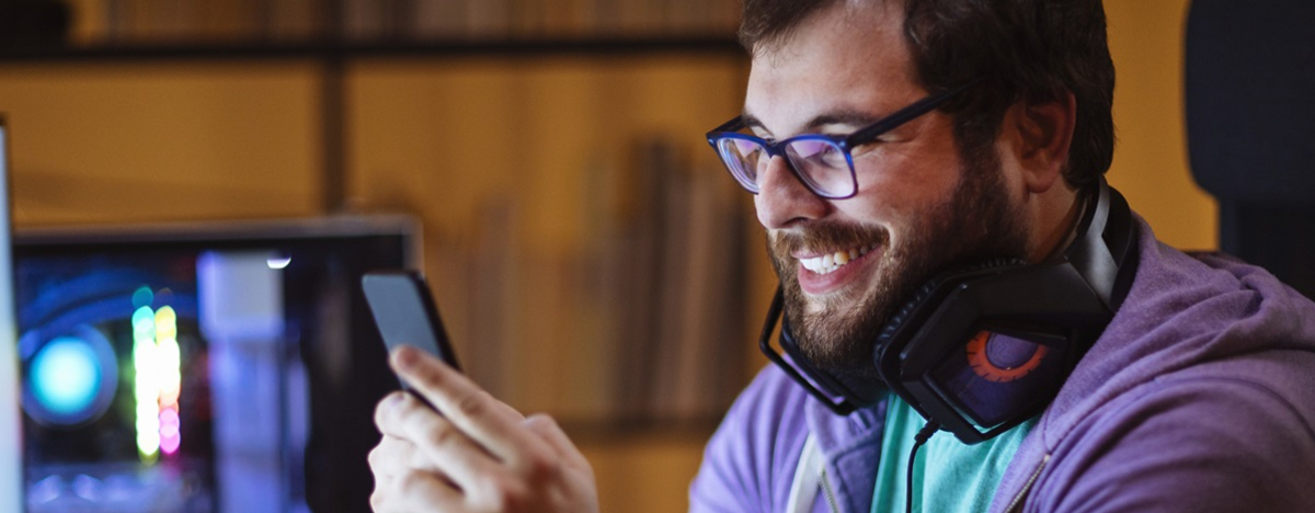 Ein nerdiger Mann mit Bart schaut auf sein Smartphone, l&auml;chelt.
