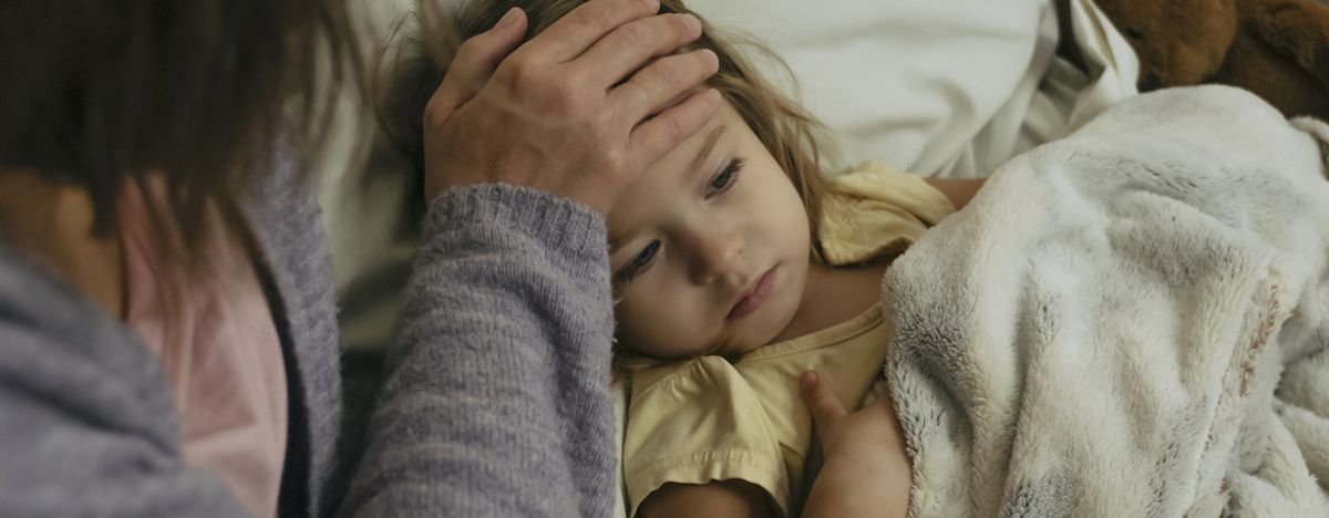 Kleines M&auml;dchen liegt krank im Bett und Mutter misst Fieber