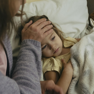 Kleines M&auml;dchen liegt krank im Bett und Mutter misst Fieber