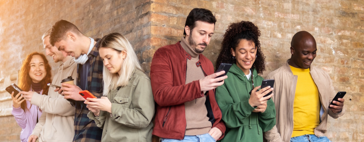 Gruppe von Personen, die an eine Wand lehnen und ihr Smartphone checken