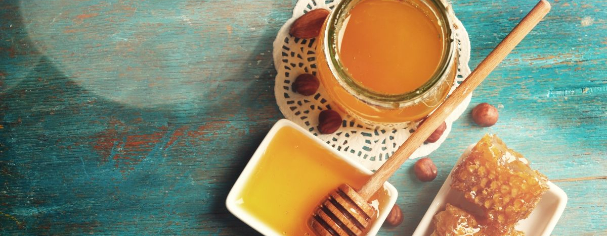 Ein Glas Honig, daneben liegt ein Honigl&ouml;ffel und zwei kleine St&uuml;cke Bienenwabe in je einer Schale.