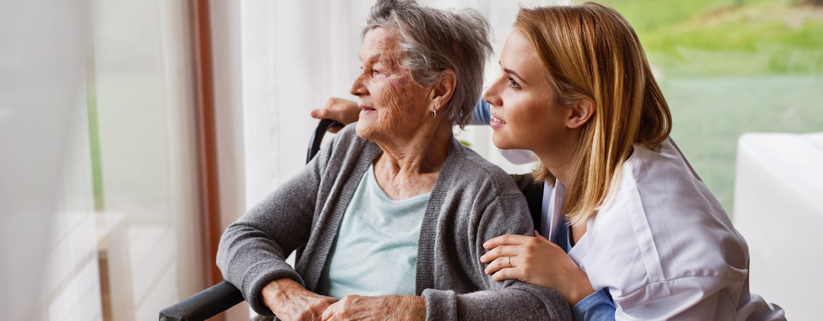 Krankenpflegerin besch&auml;ftigt sich mit &auml;lterer Dame im Rollstuhl