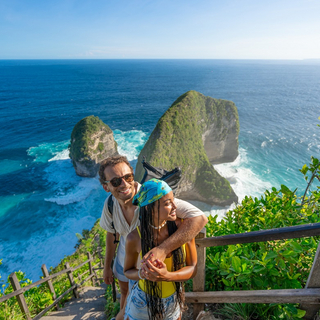 Ein gl&uuml;cklich l&auml;chelndes Paar steht auf einem Felsen vor dem Meer auf Bali.