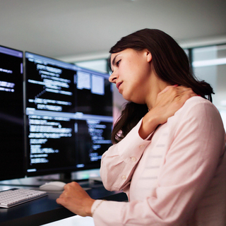 Eine junge Frau, die im B&uuml;ro sitzt und sich ihren Nacken reibt.