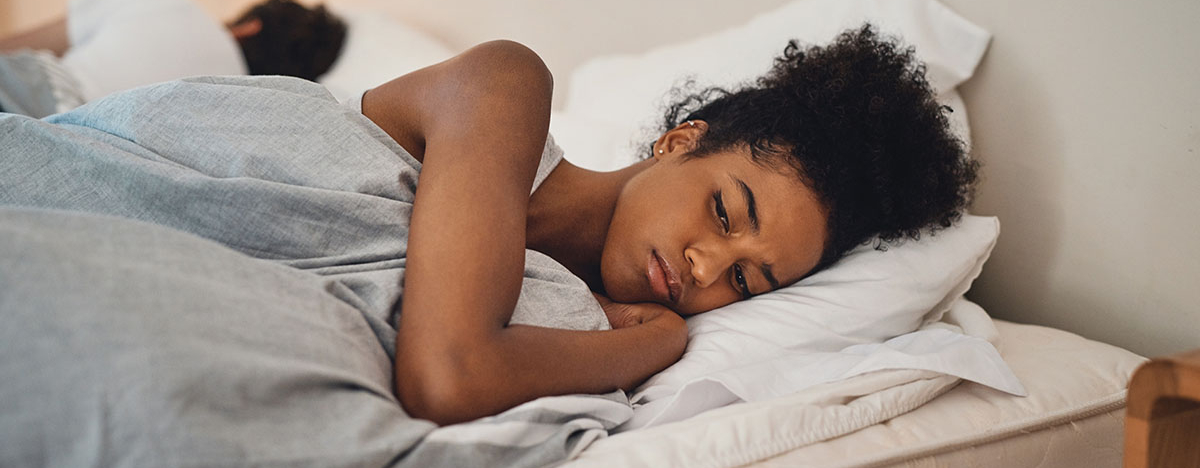 Frau liegt wach neben Mann im Bett