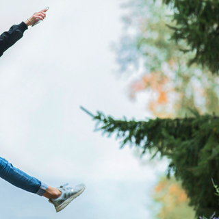 Eine Junge Frau mit Rucksack springt fr&ouml;hlich durch den Wald.