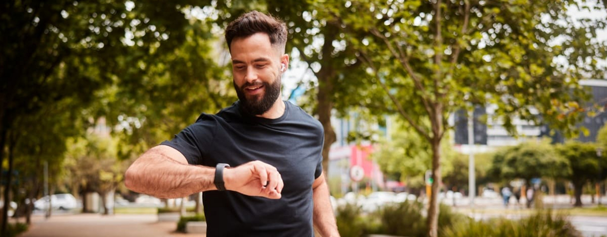 L&auml;chelnder Mann, der w&auml;hrend eines Parklaufs seinen Fitness-Tracker &uuml;berpr&uuml;ft.