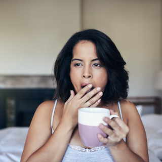 Eine Frau trinkt eine Tasse Kaffee im Bett.