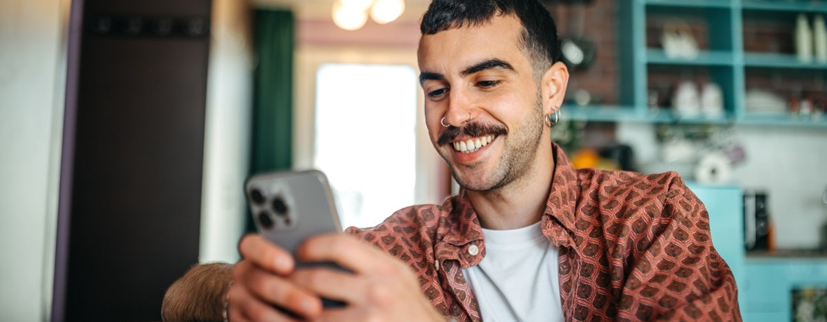Ein Hipster-Mann sitzt auf einem Sofa in seinem Wohnzimmer und &auml;ndert seine pers&ouml;nlichen Daten am Smartphone