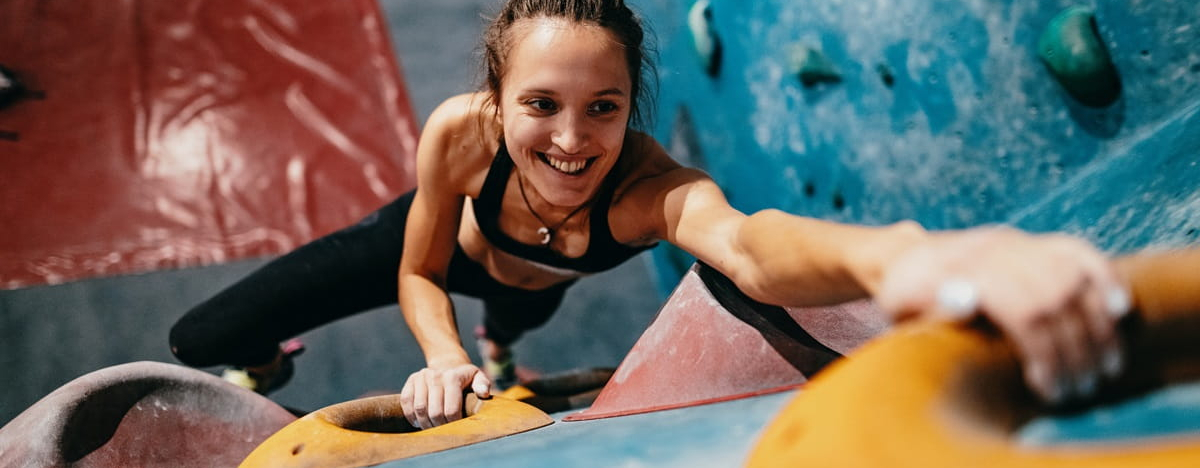 Hochwinkelansicht der d&uuml;nnen starken Frau, die auf Boulderwand klettert.