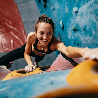 Hochwinkelansicht der d&uuml;nnen starken Frau, die auf Boulderwand klettert.