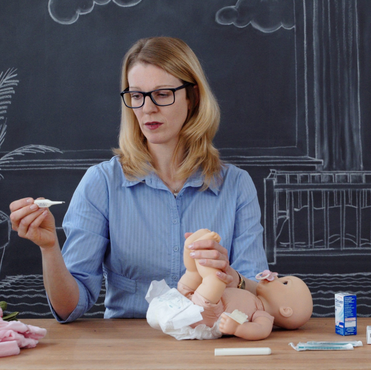 &Auml;rztin demonstriert an Puppe, wie Fiebermessen beim Baby geht