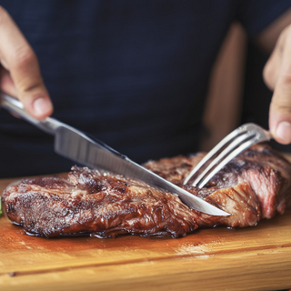 Ein St&uuml;ck Fleisch liegt auf einem Brett und wird mit Messer und Gabel geschnitten.