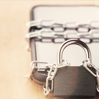 Smartphone ist mit einer Stahlkette umwickelt, die durch ein Schloss abgeschlossen wird.