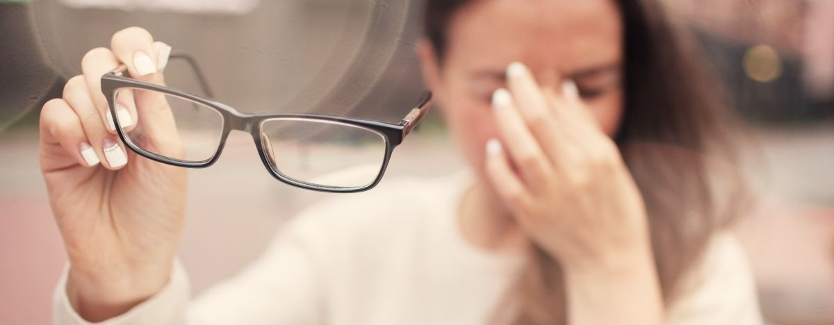 Junge Frau hat Schmerzen und nimmt sich Brille ab. 