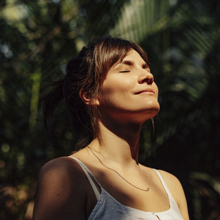 Frau steht in einem tropischen Wald und h&auml;lt ihr Gesicht in die Sonne