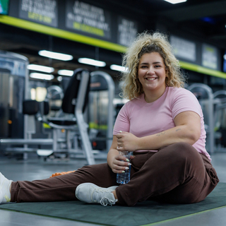 Blonde fr&ouml;hliche Frau sitzt auf einer Turnmatte in einem Fitnessstudio