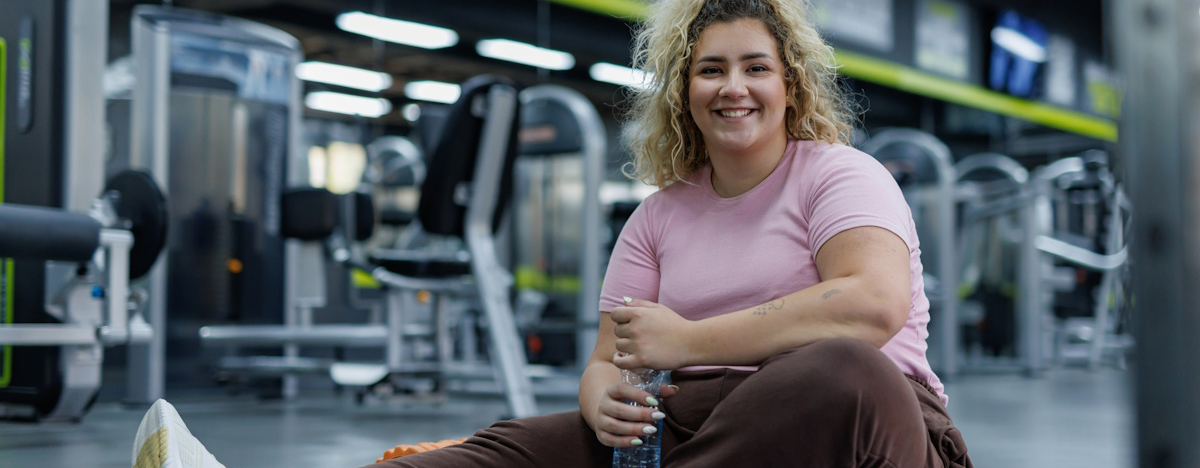 Blonde fr&ouml;hliche Frau sitzt auf einer Turnmatte in einem Fitnessstudio