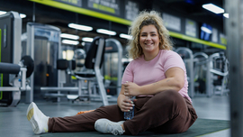 Blonde fr&ouml;hliche Frau sitzt auf einer Turnmatte in einem Fitnessstudio