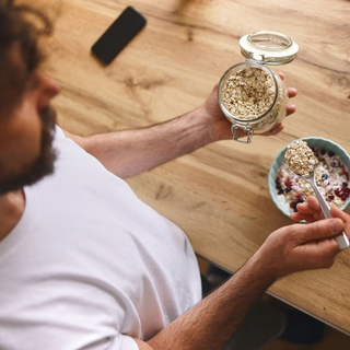 Mann bereitet zu Hause ein gesundes Fr&uuml;hst&uuml;ck mit Hafer und Beeren zu.